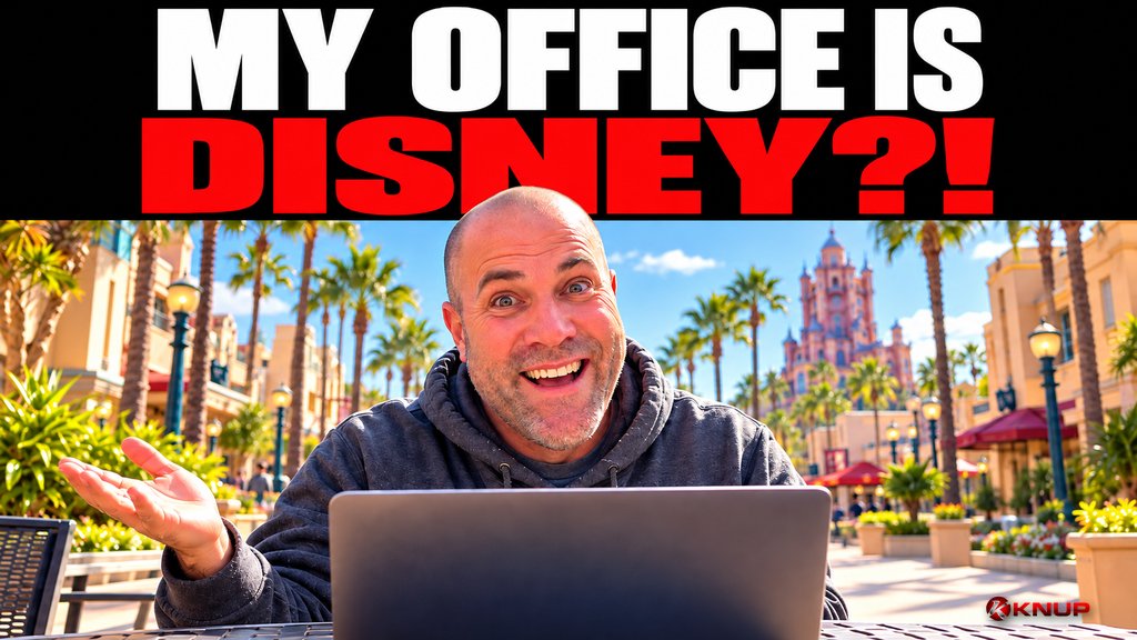 Knup grinning wide-eyed behind an open laptop at a theme park patio table, with bold red and black text reading MY OFFICE IS DISNEY?!
