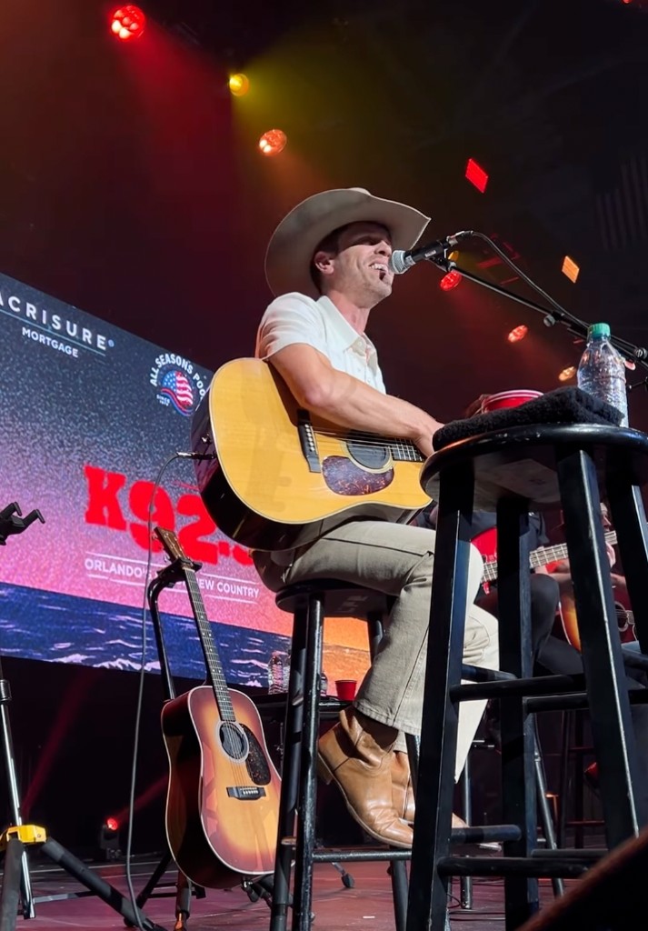 Acoustic performer on stool at All Star Jam under K92.3 backdrop