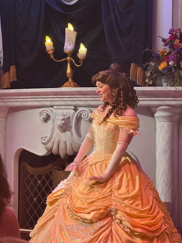 Belle performing in front of the fireplace with Lumiere