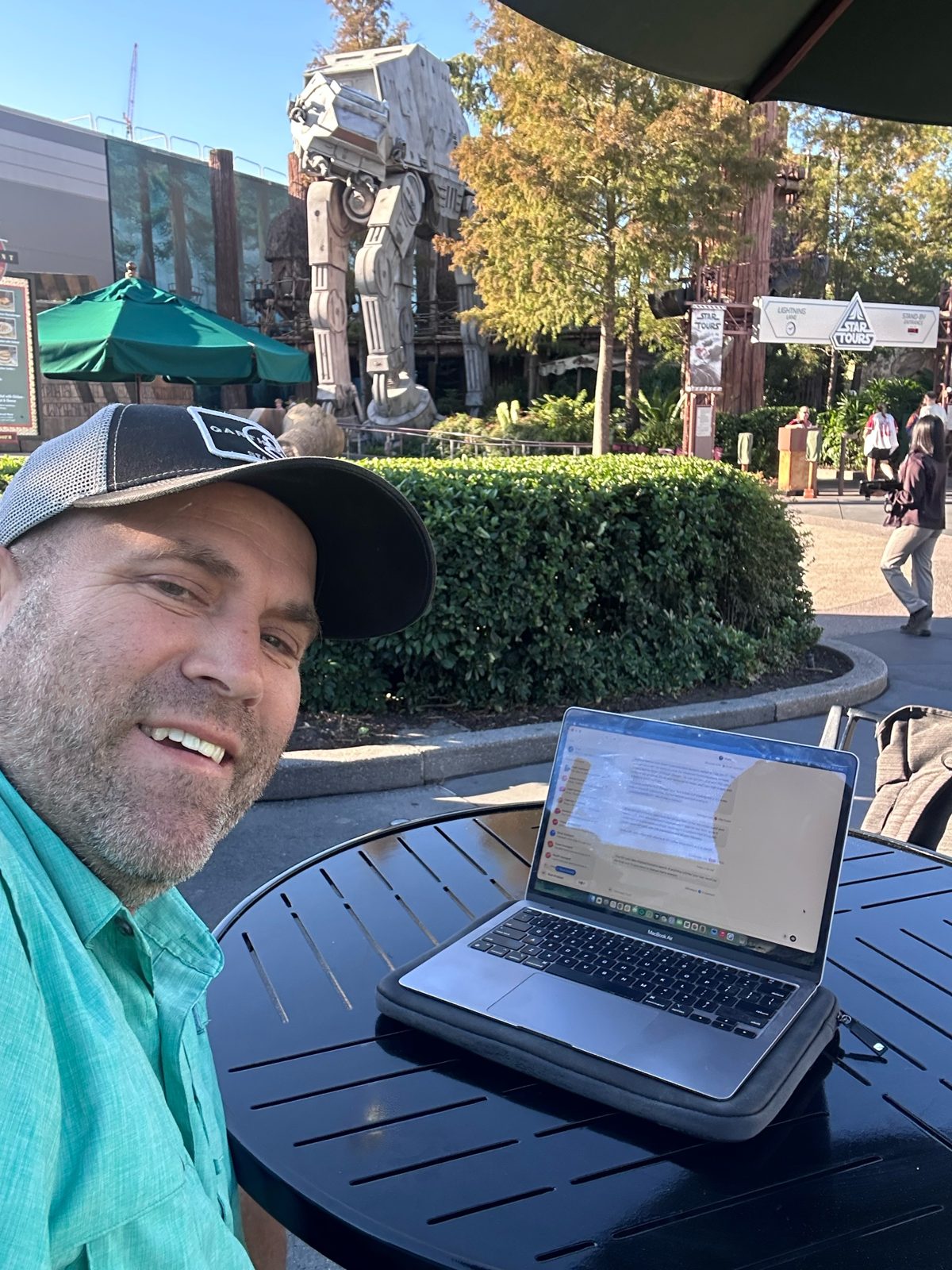 Knup with his laptop at a table at Backlot Express, the AT-AT and Star Tours sign behind him