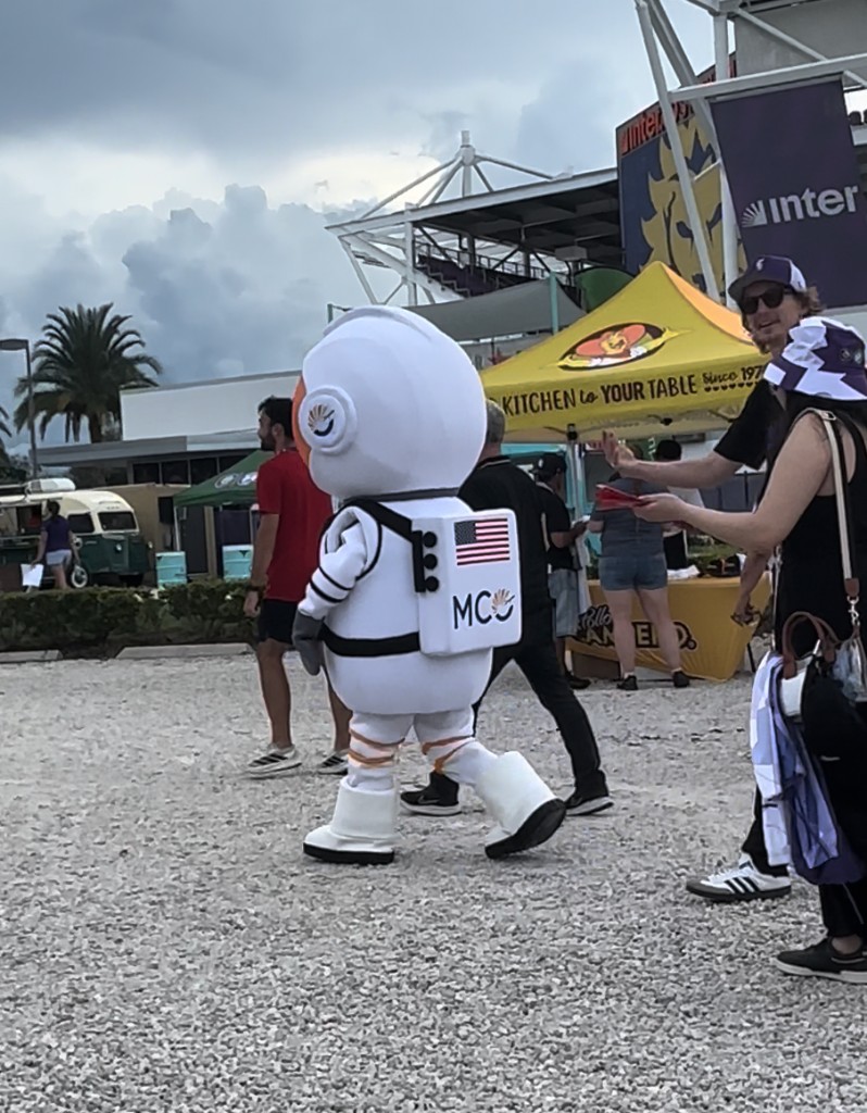 MCO astronaut walking the plaza with Inter&Co Stadium behind