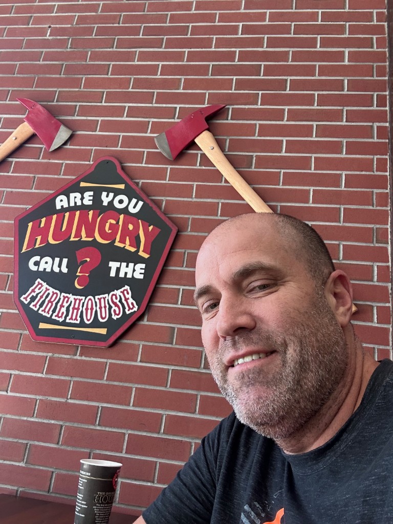 Ryan inside Firehouse Subs with brick wall and firehouse decor