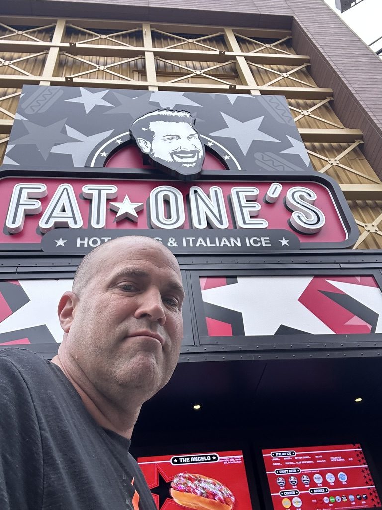 Ryan under the Fat One's sign with menu screens below
