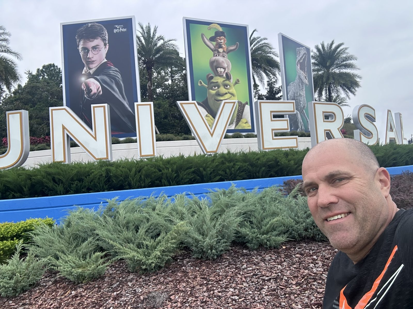 Ryan taking a selfie in front of the UNIVERSAL sign with Harry Potter, Shrek and Jurassic World banners