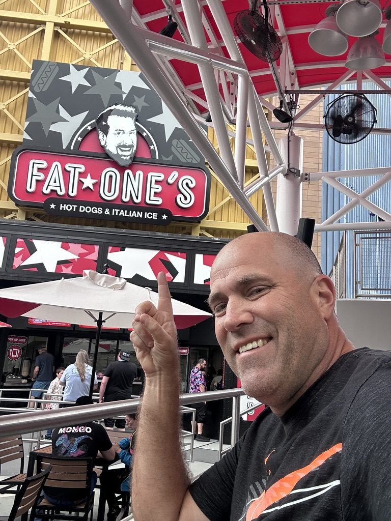 Ryan pointing up at the Fat One's Hot Dogs & Italian Ice sign